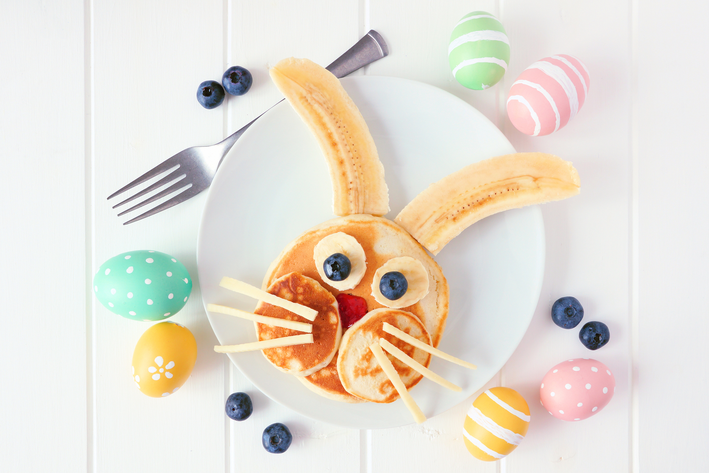 Cute Easter Bunny pancakes on a white plate. Top view against a white wood background.